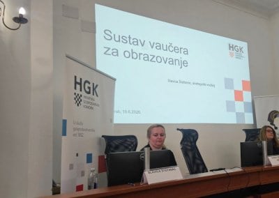 osebe sedijo za govorniškim pultom, v ozadju prezentacija